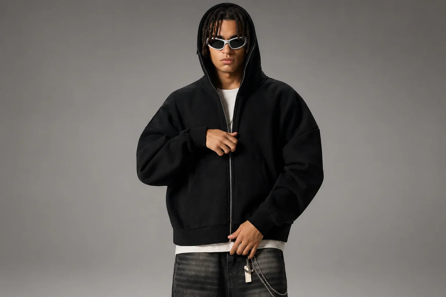 Man wearing oversized black zip hoodie, white t-shirt, dark jeans, and sunglasses