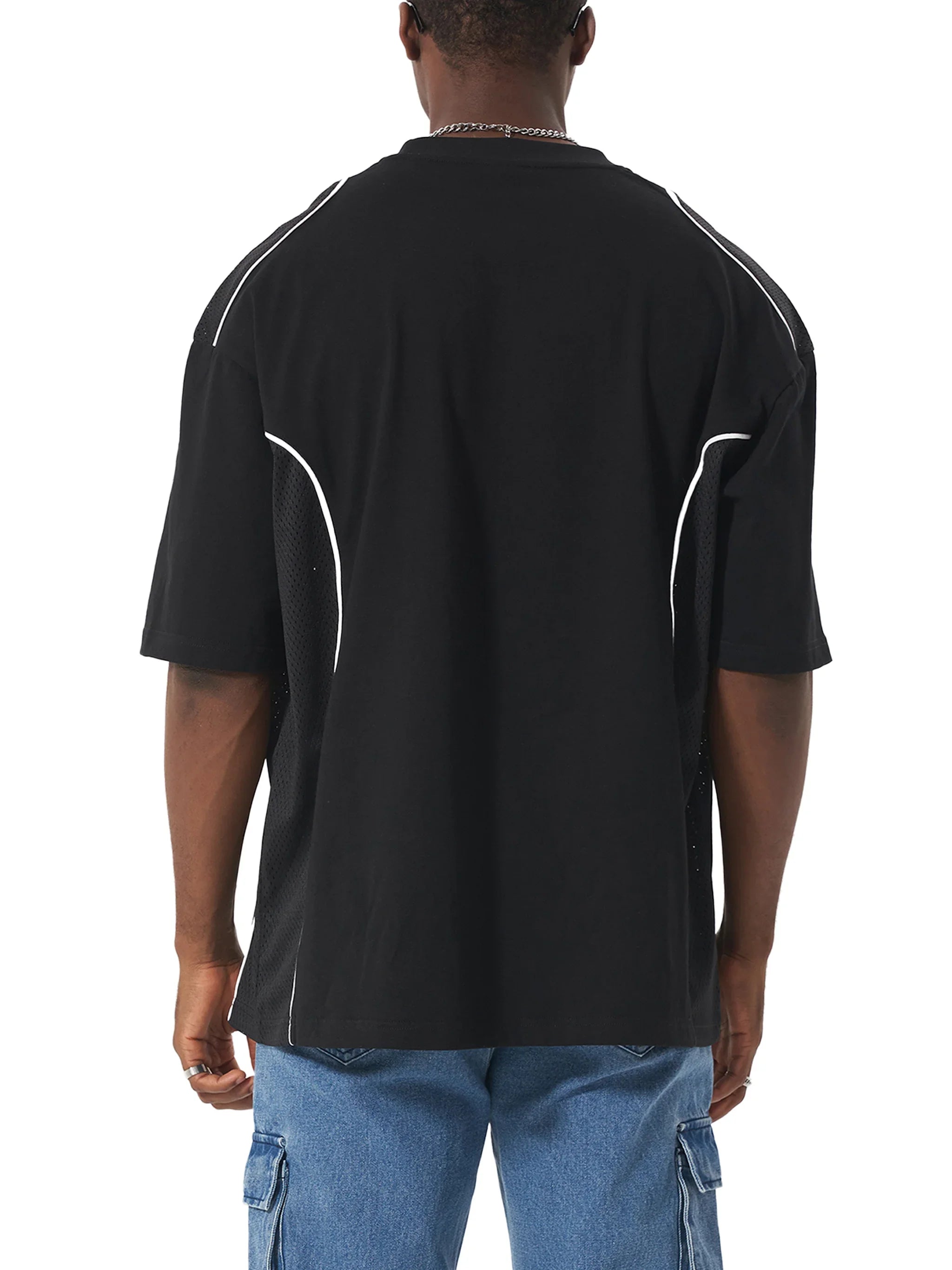 Back view of a man in an oversized black t-shirt with white piping and blue cargo jeans