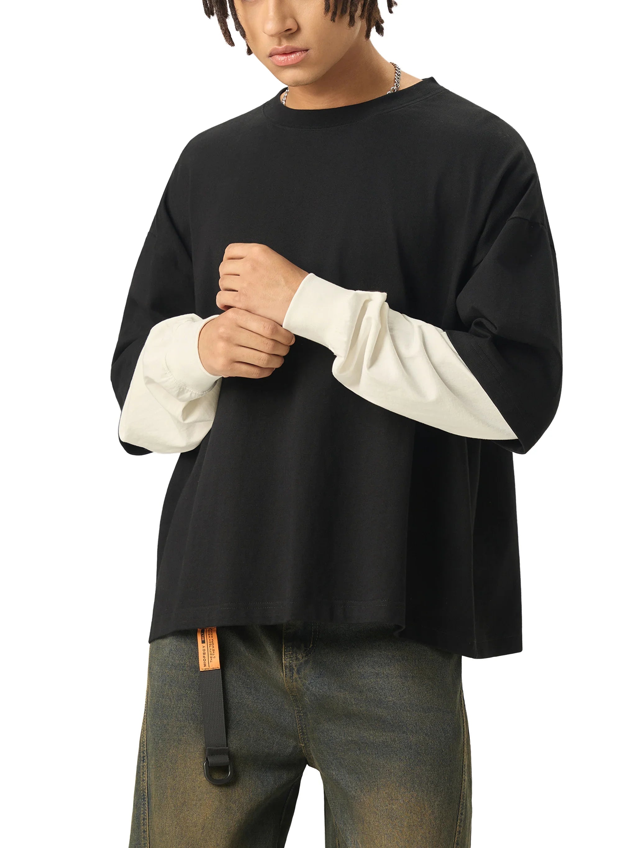 Oversized black streetwear t-shirt with contrasting white long sleeves, worn with jeans.