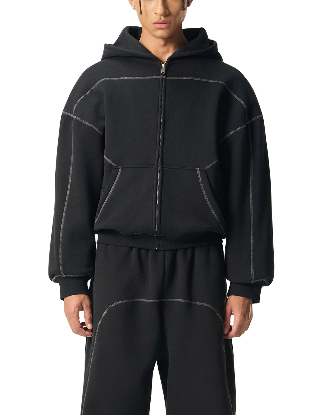Man wearing black oversized zip hoodie and matching sweatpants with contrast stitching, front view