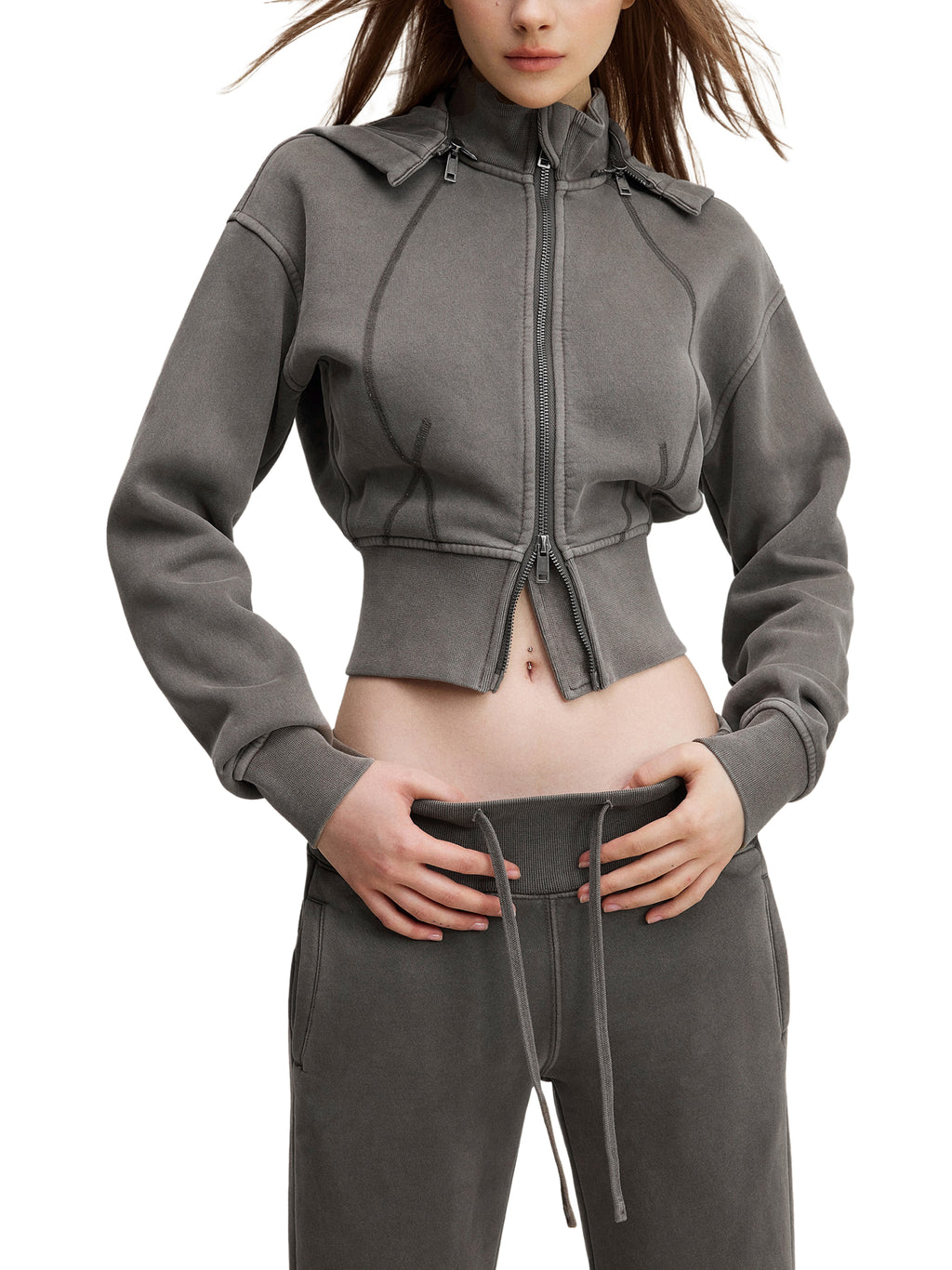 Woman wearing a cropped grey zip-up hoodie and matching joggers, urban streetwear style