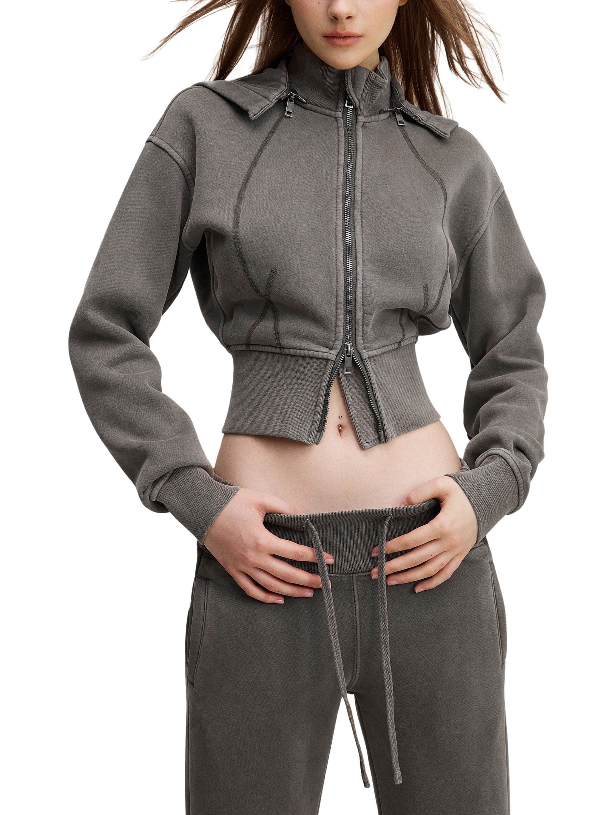 Woman wearing a cropped grey zip-up hoodie and matching joggers, urban streetwear style