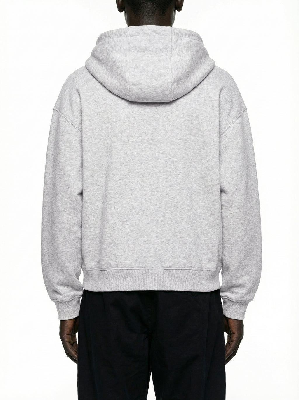Back view of a man wearing a light grey oversized hoodie and black pants on white background